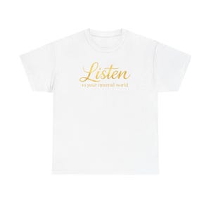May include: White t-shirt featuring the word "Listen" in gold script, with the phrase "to your internal world" underneath. The shirt has a classic crew neck.