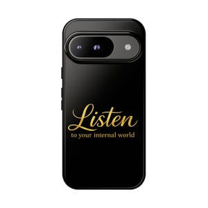 Puede incluir: Funda de teléfono negra con la inscripción dorada "Listen to your internal world". La funda tiene una cámara y un flash en la parte superior. El diseño de la funda es elegante y moderno.