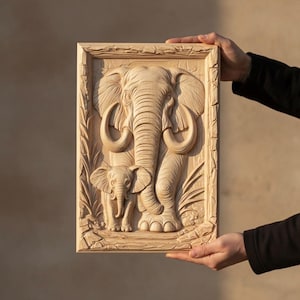 May include: A wooden relief carving of an adult elephant and a baby elephant within a rectangular frame. The carving showcases detailed features, including tusks and skin texture. The artwork is presented in a natural wood tone, highlighting the carved details.