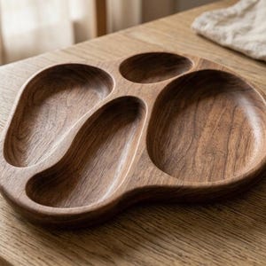 Könnte beinhalten: Ein Serviertablett aus Holz mit vier Fächern. Das Tablett ist aus dunkelbraunem Holz gefertigt und hat eine glatte, polierte Oberfläche. Die Fächer haben verschiedene Formen und Größen, ideal zum Servieren von Snacks oder Vorspeisen. Das Tablett steht auf einem Holztisch.