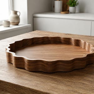 Könnte beinhalten: Ein rundes Holztablett mit gewelltem, gebogtem Rand und einer glatten, natürlich braunen Holzmaserung. Das Tablett verfügt über eine flache Innenseite und ein durchgehend geschwungenes Randdesign, das die organische Textur des Holzes hervorhebt.