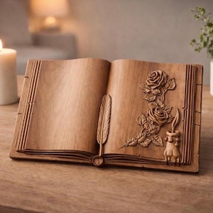 Può includere: Libro di legno aperto con rose intagliate, una piuma e una candela. Il libro è su un tavolo di legno, con una candela accesa e una pianta in vaso sullo sfondo. Le pagine del libro sono vuote.