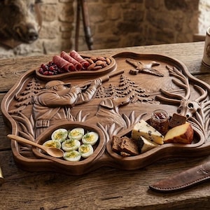 May include: A wooden serving tray with carved hunting scene details, holding food items like deviled eggs, meats, and cheeses. The tray is surrounded by hunting-themed accessories, including mugs, binoculars, and a compass, all set on a rustic wooden table.