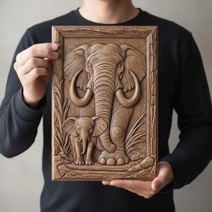 May include: A detailed wooden relief carving of an elephant and its calf, set within a rectangular frame. The artwork showcases the elephants with intricate details, including tusks and textured skin. The piece is held by a person, highlighting the craftsmanship.