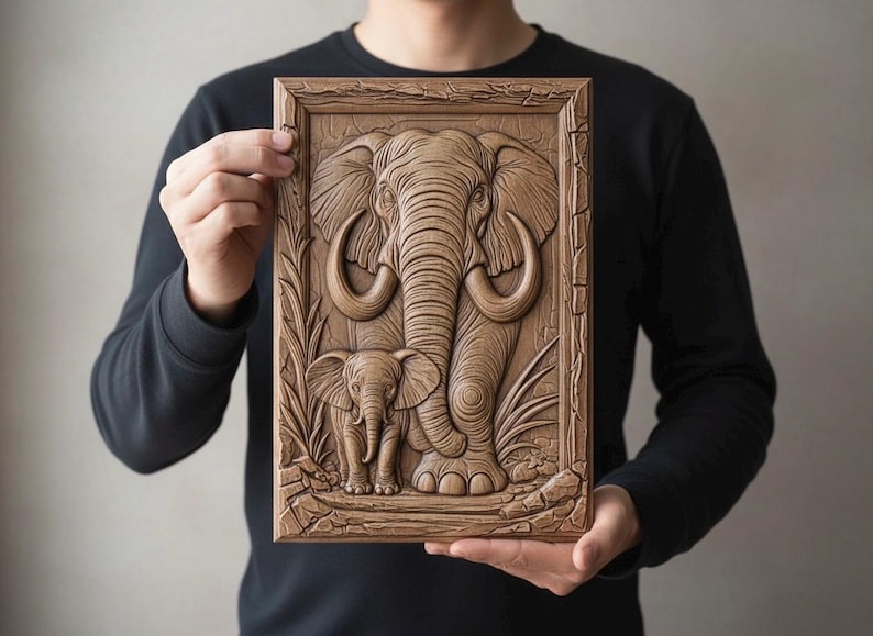 May include: A detailed wooden relief carving of an elephant and its calf, set within a rectangular frame. The artwork showcases the elephants with intricate details, including tusks and textured skin. The piece is held by a person, highlighting the craftsmanship.