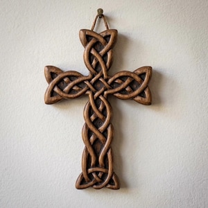 May include: A wooden Celtic cross with intricate knotwork design. The cross is a warm brown color and hangs from a small loop. The detailed carving is visible, showcasing the craftsmanship of the piece. The cross is a symbol of faith and spirituality.