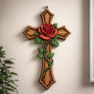 May include: Wooden cross featuring a carved red rose and green leaves. The cross is a medium brown colour, and the rose is a vibrant red. The leaves and stem are green. The cross is hanging on a white wall.