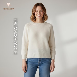 May include: Cream-colored sweater with the text "FLOW SWEATER" in a vertical font. The sweater has a crew neck and long sleeves. The model is wearing blue jeans. The brand logo "OPALLOOP" is in the upper left corner.
