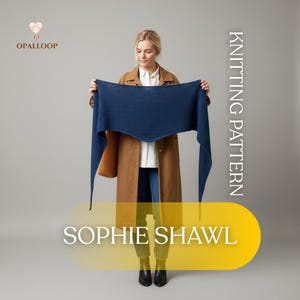 May include: A woman holds up a navy blue Sophie Shawl knitting pattern. The shawl is a triangular shape with long, pointed ends. The text "Knitting Pattern" is on the right side of the image, and "Sophie Shawl" is at the bottom.