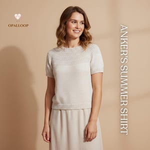 Puede incluir: Una mujer con una camiseta de punto beige claro de manga corta y una falda a juego. La camiseta tiene un cuello de canalé y un diseño de canalé horizontal en el pecho. El texto "ANKER'S SUMMER SHIRT" es visible en el lado derecho.