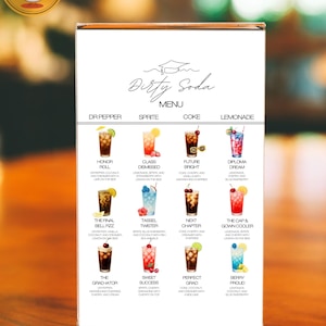 May include: A clear acrylic menu stand displaying a "Dirty Soda" menu with various colorful drink illustrations. The menu features drink names like "Honor Roll" and "Diploma Dream" with ingredient descriptions. The stand is on a wooden surface.