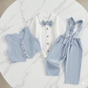 May include: A three-piece outfit consisting of a white short-sleeved collared bodysuit with a light blue bow tie, a light blue button-up vest, and matching light blue trousers with attached suspenders, all featuring small brown buttons.