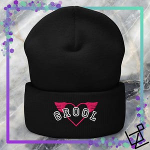 Puede incluir: Gorro negro con la palabra "GROOL" bordada en blanco, dentro de un corazón rosa con alas rosas. El gorro está hecho de un material suave y tejido.