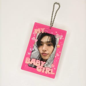 Op de afbeelding: Een roze rechthoekige sleutelhanger met een foto van een persoon in een grijze hoodie. De sleutelhanger heeft de roze tekst "MY BABY GIRL". Versierd met roze strikken, hartjes, sterren, een cupcake en een kers.