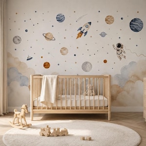Op de afbeelding: Een muurschildering met een aquarelruimtethema met planeten, sterren, een raket en een astronaut. Het ontwerp bevat zachte blauwe en beige wolken aan de basis, wat een hemelse scène creëert op een lichte muur achter een houten ledikant.