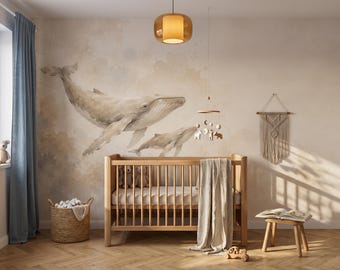 Puede incluir: Una cuna de madera con una manta de color claro, colocada contra una pared con un gran mural de acuarela de dos ballenas. La habitación incluye una cesta tejida, un móvil colgante, un tapiz de macramé y un pequeño taburete de madera con un libro.