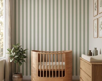 Puede incluir: Una cuna ovalada de madera clara con barrotes verticales y un colchón blanco, situada en una habitación con papel pintado de rayas verticales en verde salvia y blanco, una cómoda de madera, una planta en maceta y una alfombra acolchada.