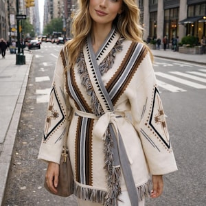 May include: Cream wrap cardigan with geometric patterns in brown, grey, and black. The cardigan has fringe detailing and a matching belt. A stylish outerwear piece for a casual look.