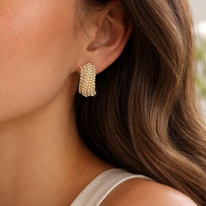 May include: Gold-toned hoop earrings encrusted with small, white, round stones. The earrings are rectangular in shape and are worn on the ear. The earrings are a jewelry item.