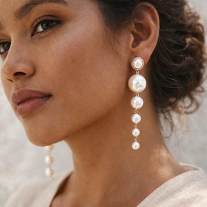 May include: Elegant gold-tone earrings featuring a cascade of white pearls. The earrings have a graduated design, with the pearls decreasing in size from top to bottom. The earrings are a classic accessory.