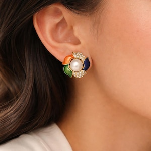 May include: A gold-toned stud earring featuring a central white pearl surrounded by colorful enamel petals in orange, green, and blue. The petals are accented with small, sparkling crystals, creating a vibrant and elegant design.