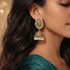 May include: Gold-toned drop earrings with a teardrop-shaped top, adorned with small, white pearls. The earrings feature a detailed, bell-shaped bottom with dangling pearls. The design is intricate and ornate, suitable for special occasions.