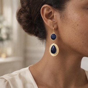 Puede incluir: Pendientes colgantes dorados con una piedra redonda azul oscuro en la parte superior y una piedra en forma de lágrima en la parte inferior. Los pendientes tienen un borde dorado texturizado y un cierre de gancho. Un accesorio de joyería clásico.