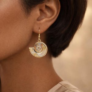 May include: Gold-toned seashell earrings with a spiral design. The earrings feature a detailed, textured surface with a gold-colored frame and a hook closure. The earrings are a unique accessory.