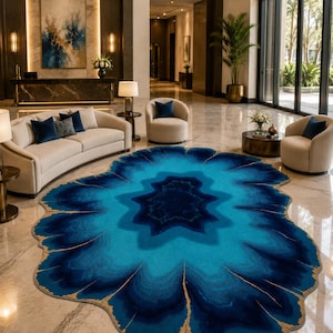 Può includere: Un tappeto dalla forma organica irregolare caratterizzato da strati concentrici di blu navy profondo, blu reale e turchese brillante, accentuato da sottili venature dorate frastagliate che imitano l'aspetto di una fetta di agata naturale.