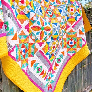 May include: A handmade quilt featuring a vibrant patchwork design with geometric star and floral patterns in bright yellow, pink, orange, teal, and blue. The quilt has a solid yellow border with swirling quilted stitching and black and white striped accents.