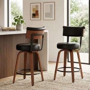 Könnte beinhalten: Zwei moderne Barhocker mit schwarzen Sitzflächen und Rückenlehnen sowie Holzbeinen. Die Hocker haben ein geschwungenes Design und eine Metallfußstütze. Der Hintergrund zeigt eine Küchenumgebung mit Arbeitsplatte, Pflanzen und Kunstwerken.