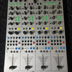 Puede incluir: Mesa de mezclas de audio electrónica plateada con numerosas perillas, botones y controles deslizantes. Cuenta con botones iluminados en verde, amarillo y rojo. El texto "4 midi loop" es visible en la parte inferior, junto con "powered by faderfox".
