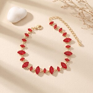 May include: A gold-tone bracelet featuring a series of marquise-cut red crystals linked together. The jewelry piece includes a delicate chain segment with a lobster claw clasp and an adjustable extender chain to customize the fit for the wearer.
