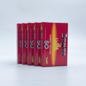 May include: A stack of five red cassette tape boxes. The boxes have the word "Zapas" in white, with "NORMAL POSITION" and "50" printed on the front. The boxes are for audio recording.