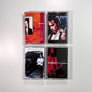 Może przedstawiać: Cztery kasety magnetofonowe z okładkami albumów Jeffa Buckleya. Kasety mają różne schematy kolorów, w tym pomarańczowy, niebieski i czerwony. Każda kaseta wyświetla imię i nazwisko artysty oraz tytuły albumów ze zdjęciami Buckleya.