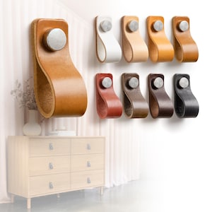 Może przedstawiać: Kolekcja skórzanych uchwytów do szafek w różnych kolorach, w tym brązowym, białym i czarnym, z srebrnym metalowym akcentem. Uchwyty są zamontowane na białej ścianie, z drewnianą komodą w tle. Zaprojektowane jako uchwyty do szuflad.