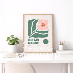 Puede incluir: Una impresión artística enmarcada con una flor rosa y hojas verdes, con el texto "All My Heart". La obra de arte está en un marco de madera clara y se exhibe en un escritorio blanco con una pequeña planta en maceta y útiles de oficina.
