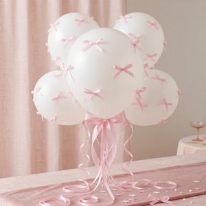 May include: A cluster of white balloons adorned with small pink bows. The balloons are tied together with pink ribbons and bows, creating a festive arrangement. Perfect for a party or celebration.
