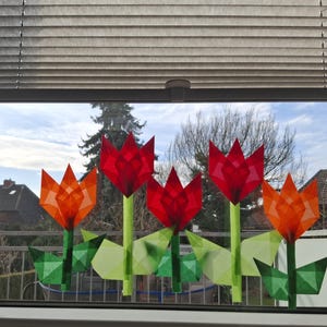 Könnte beinhalten: Fensterdekoration mit fünf Papiertulpen in Rot- und Orangetönen. Die Tulpen haben grüne Stiele und Blätter. Das Fenster blickt auf ein Wohngebiet mit einem bewölkten Himmel, der durch das Glas sichtbar ist.