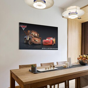 May include: A framed canvas print featuring the animated characters Mater and Lightning McQueen from the Disney Pixar Cars movie. The print shows the two cars against a dark background, with the text "MATER & LIGHTNING MCQUEEN" below.