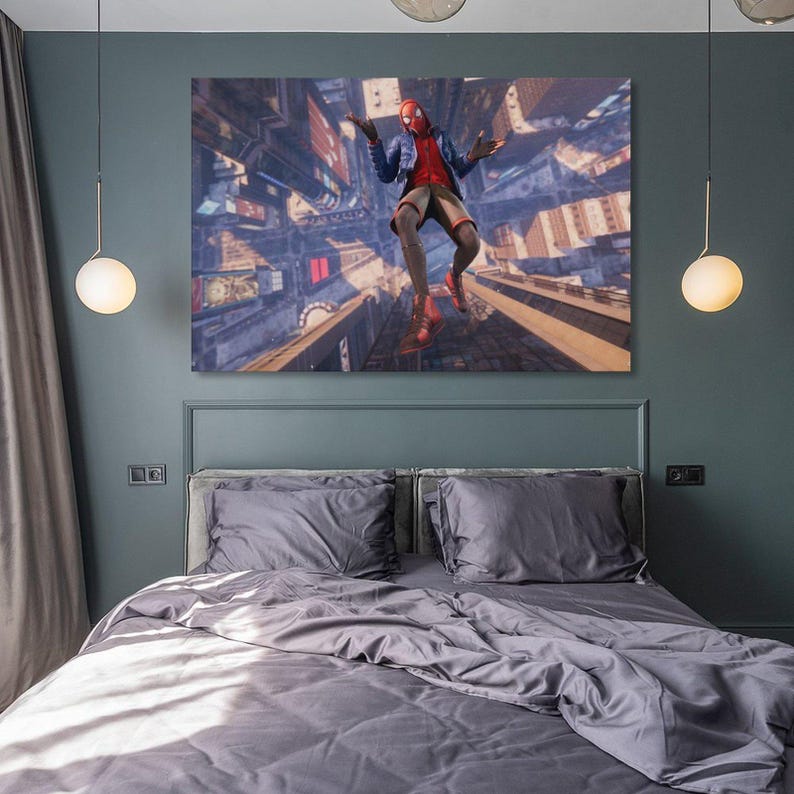Puede incluir: Un lienzo de un superh&eacute;roe con un traje rojo y negro, en el aire sobre un paisaje urbano. La obra de arte se exhibe sobre una cama con ropa de cama gris, contra una pared verde oscuro. La habitaci&oacute;n est&aacute; iluminada por dos l&aacute;mparas colgantes.