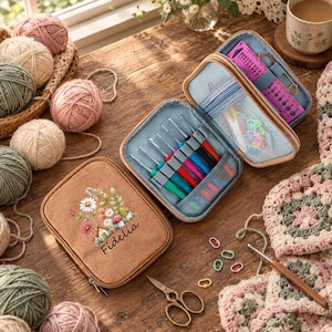 May include: A tan zipped crochet hook case featuring a floral and mushroom illustration with the name Fidelia printed in black. The open case reveals multiple colourful crochet hooks, a purple gauge tool, and mesh pockets with small notions.