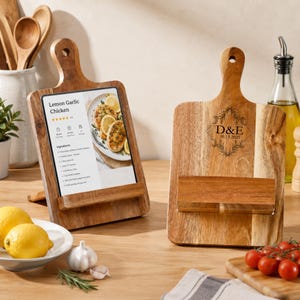 Könnte beinhalten: Zwei hölzerne Rezeptständer mit Griff. Einer zeigt ein Rezept für Zitronen-Knoblauch-Hähnchen. Der andere hat die Initialen "D&E" und das Datum "10.13.2025" eingraviert. Die Ständer stehen auf einer Holzoberfläche mit Zitronen, Knoblauch und Tomaten.