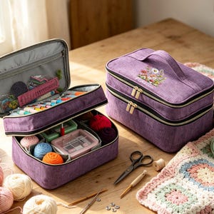 May include: Two purple fabric storage cases for craft supplies. One case is open, revealing compartments filled with colourful yarn balls, a plastic container, and crochet hooks. The closed case features a floral print and the name Fidelia.