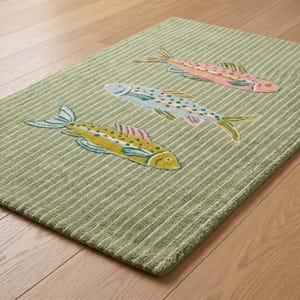 May include: A rectangular sage green rug featuring a textured surface with thin white vertical stripes. The rug is decorated with three embroidered fish motifs in shades of pink, light blue, and yellow, each displaying detailed fins and scales.