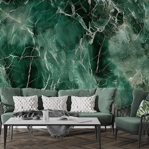 May include: A living room scene featuring a green sofa with white patterned pillows, a matching armchair, and a white coffee table. The backdrop is a large, textured green marble wall. The room has a modern, elegant aesthetic.