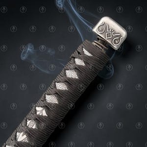 May include: A sword handle wrapped in dark gray cord over a white textured base, featuring a metallic pommel with an engraved geometric design. Wisps of smoke rise from the handle, which is set against a dark background with a repeating logo.