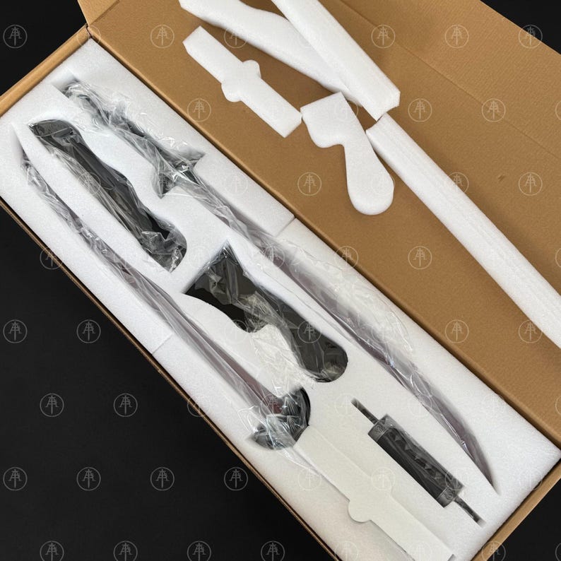 May include: A disassembled sword set packaged in a brown cardboard box with white foam inserts. The set includes a long blade, a handle, and a crossguard, all individually wrapped in clear plastic. The foam is molded to fit each component securely.