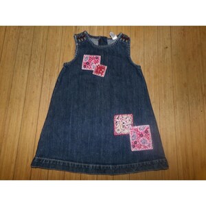 Op de afbeelding: Een mouwloze jurk van donkerblauwe denim met een ronde halslijn en een uitlopend silhouet. De jurk is versierd met vier vierkante stoffen patches in roze, rode en witte tinten, voorzien van ingewikkelde bloemen- en paisleymotieven.