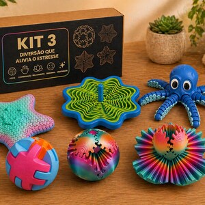 Puede incluir: Una colección de juguetes coloridos para aliviar el estrés, que incluye un pulpo azul, una estrella de mar y una bola con piezas entrelazadas. La caja dice "KIT 3 DIVERSÃO QUE ALIVIA O ESTRESSE". Los juguetes están colocados sobre una superficie de madera.